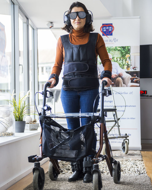 Person im Anzug zur Alterssimulation testet mit einem Rollator den Parcours.