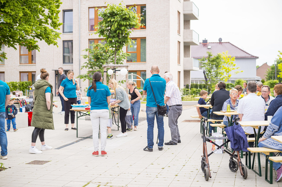 Mitarbeiterinnen und Mitarbeiter der TRAVE bei einem Mieterfest. In einem schönen Innenhof der Artlenburger Straße sitzen die Menschen an Tischen und stehen in Gruppen zusammen und reden miteinander.