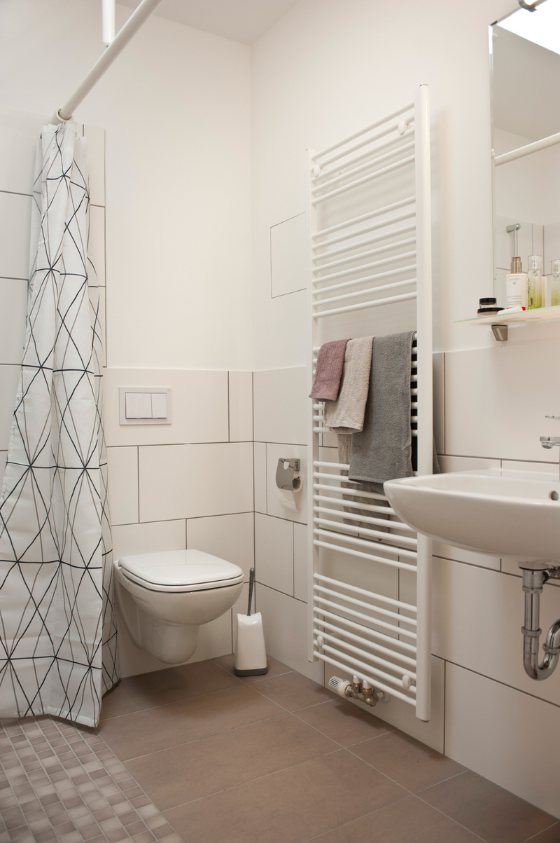 Bad mit ebenerdiger Dusche, Toilette, Handtuchheizkörper, Waschbecken.