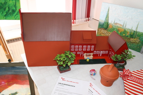Ein gebasteltes Modell von einem Haus steht auf einem Tisch zusammen mit weiteren Gegenständen. Davor liegt ein Monatsplan mit Aktivitäten im Trave-Treff. Ein gebasteltes Modell von einem Haus steht auf einem Tisch zusammen mit weiteren Gegenständen. Davor liegt ein Monatsplan mit Aktivitäten im Trave-Treff.